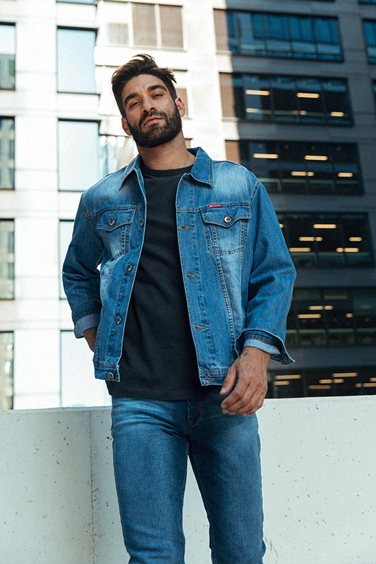 Mężczyzna w jeansach stojący na tle nowoczesnych budynków w sesji reklamowej